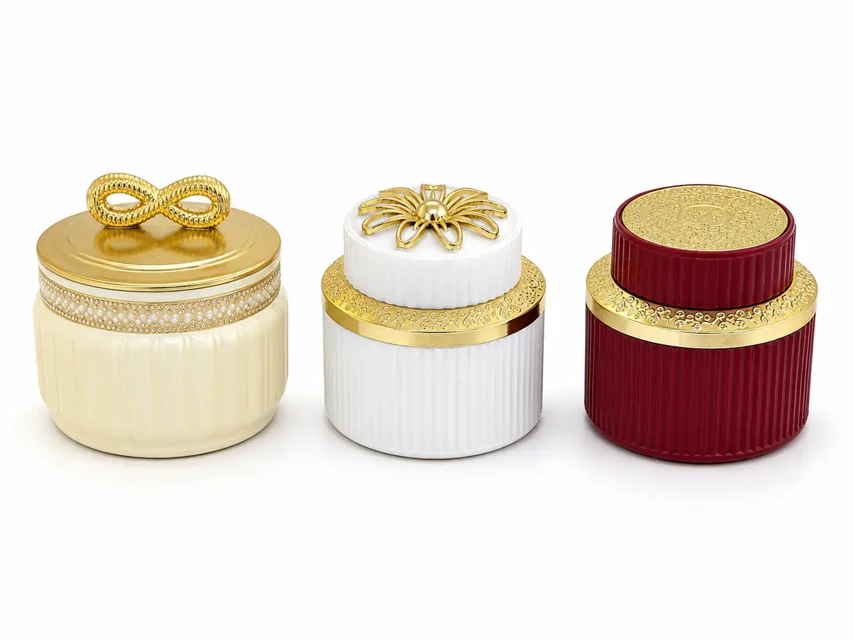 Three decorative containers in cream, white and maroon with gold metallised lids and trims